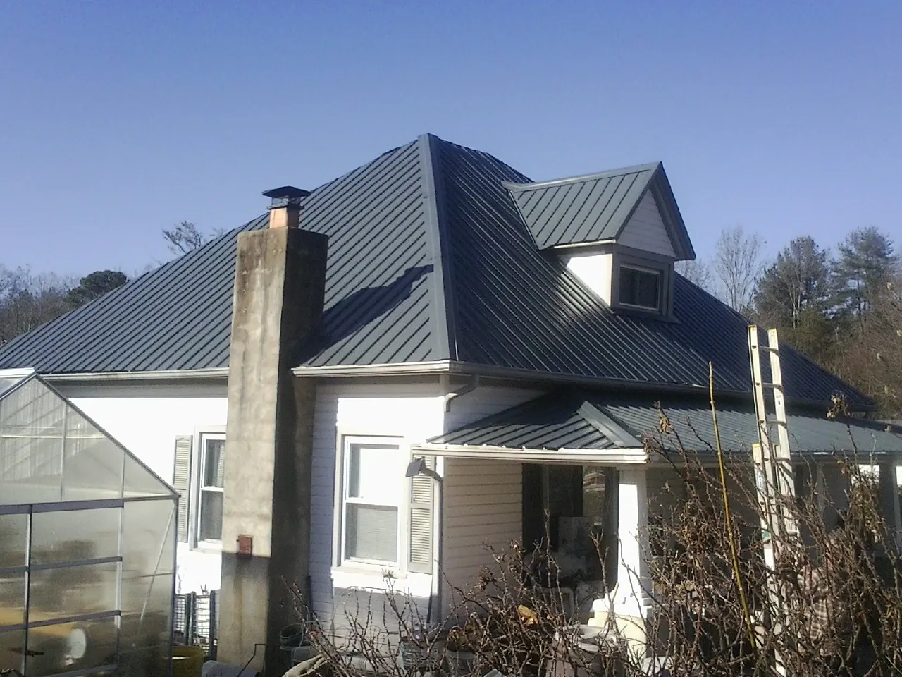 Dark blue standing seam metal roof on a white farmhouse with dormer — Slate & Tile Roof Repair by Roofing Brothers in Crescent City