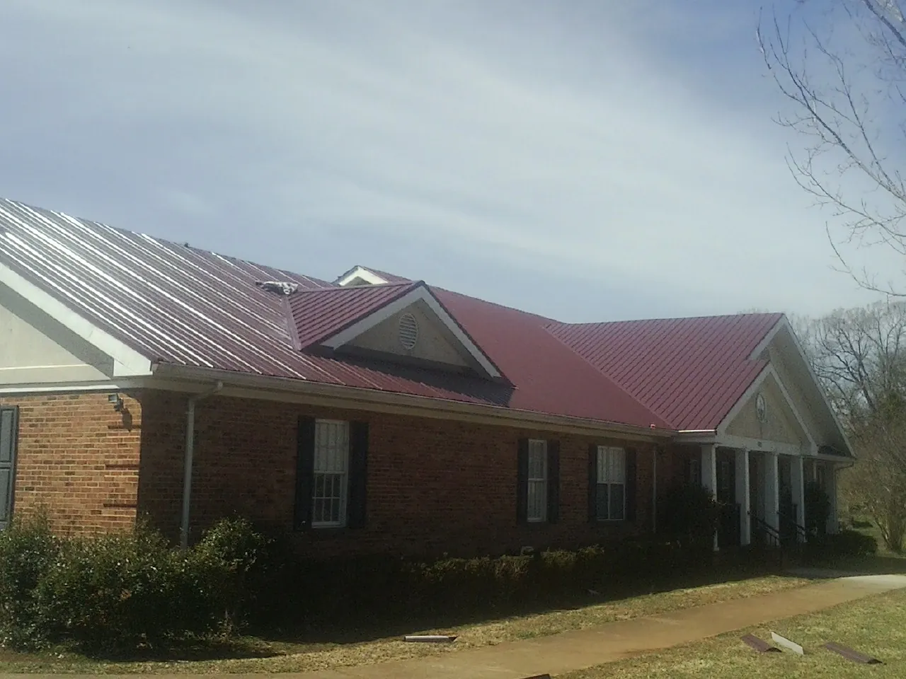 Red metal roof with gabled entries on a long brick building, from a Hail Damage Roof Repair job in Crescent City