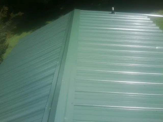 New green metal panels meeting at the ridge of a roof — Flat Roof Repair work by our crew in Crescent City