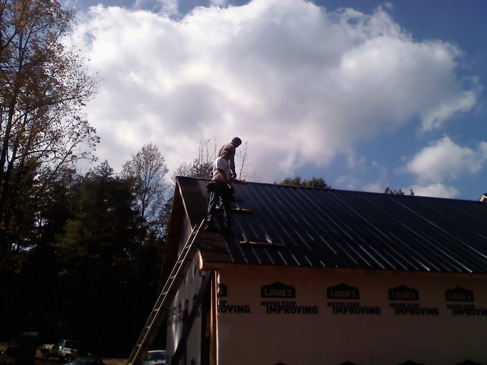 Roofer fastening dark metal panels high against a cloudy sky, from a Roof Inspection job in Crescent City