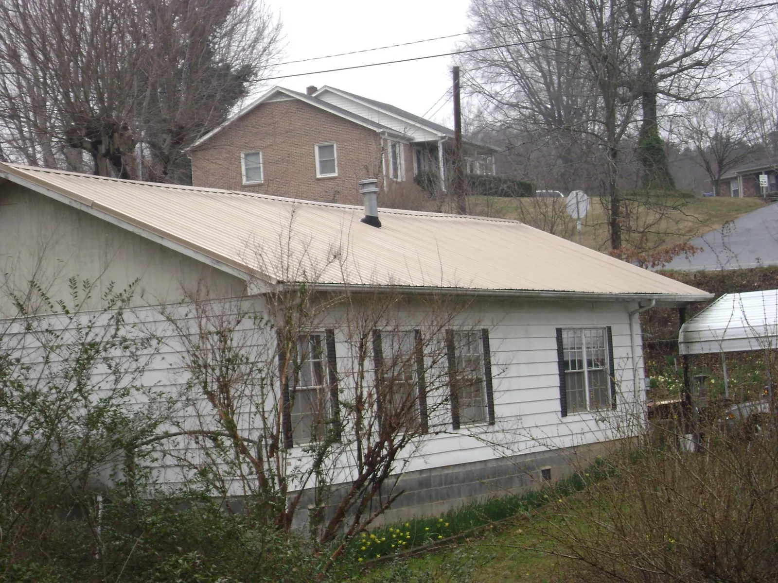Tan metal roof on a white sided house set into a hillside — Commercial Roofing by Roofing Brothers in Crescent City