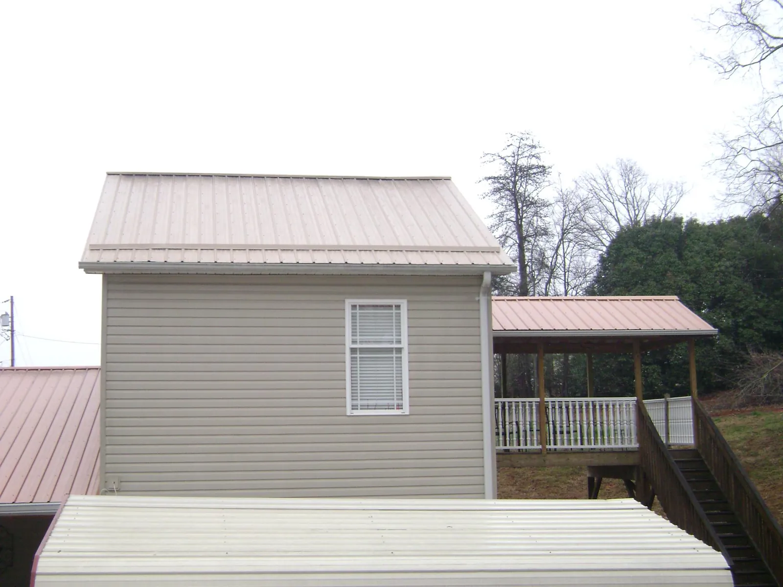 Tan metal roofs on a two story addition and attached porch, from a Roof Replacement job in Crescent City